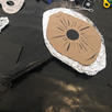 On a table is a sign made from foil, cardboard, and black tape. It has been shaped to look like an eye. 