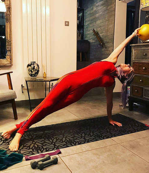 pilates instructor in red jumpsuit demonstrating side plank exercise