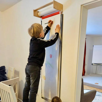 Kinder malen gemeinsam an einer wandmontierten Papierrolle.