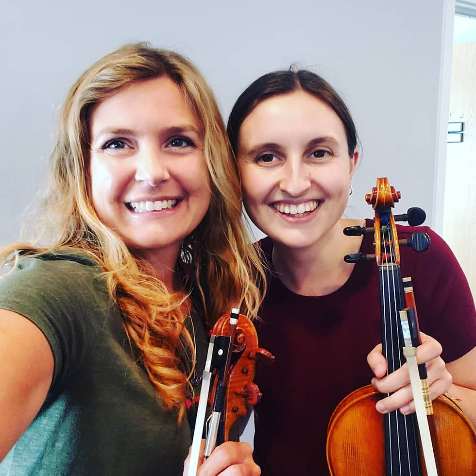 Photo of an instructor and student with their violins in their hands, smiling at the camera to take a selfie.