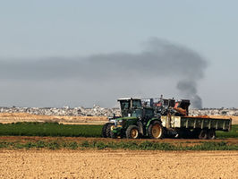 Un tracteur israélien passe dans un champ, tandis qu'au loin de la fumée s'échappe de Gaza, sous les bombes