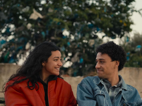 Une jeune femme habillée en rouge et un jeune homme habillé en bleu sont assis sur un banc et se regardent en souriant