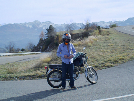 Un homme remettant sa chemise devant sa moto sur une route en montagne. 