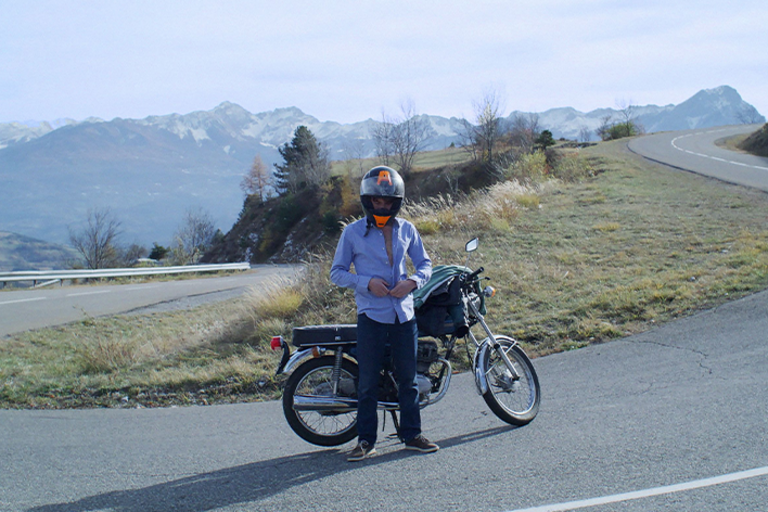 Un homme remettant sa chemise devant sa moto sur une route en montagne. 