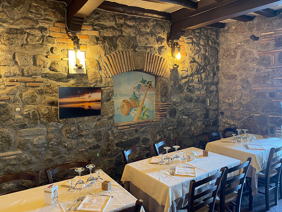 Cozy setting with stone walls, an arched niche adorned with decorations and framed artwork, tables dressed in white linens and wooden chairs, and atmospheric lighting.