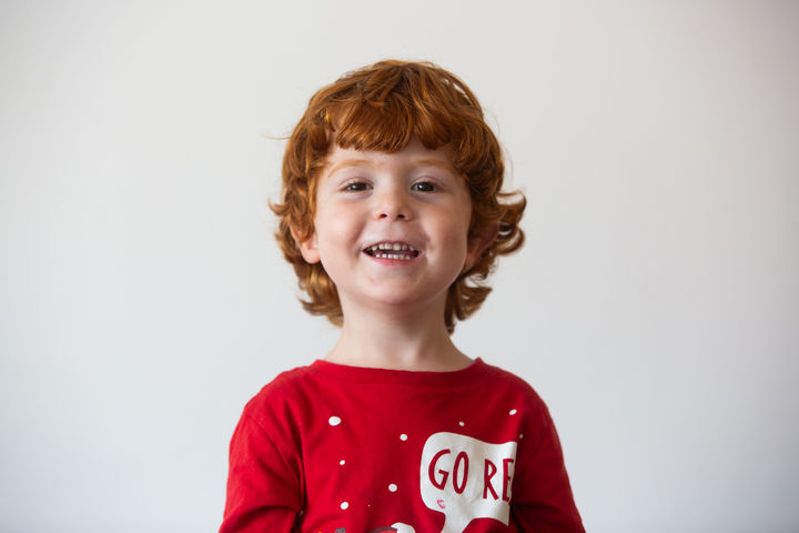 Smiling red-haired child in a red shirt. Portrait by Dafna Talmon