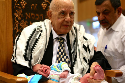 An elderly man holding a crying baby during a ceremony.