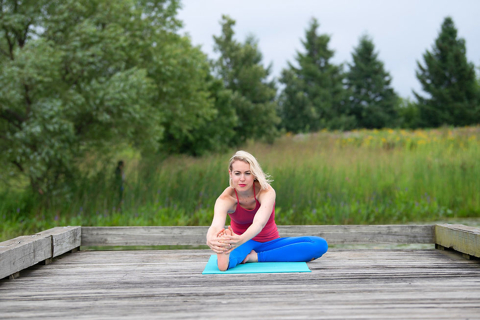 Woman with bright pink yoga top and blue yoga pants on a teal yoga mat on a wood deck with green trees in the background