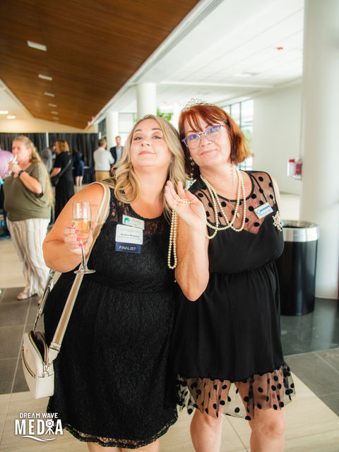 Two women smile at the camera while holding champagne PHOTOGRAPHY at conference.