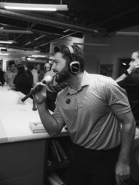 Man with beard holding microphone, wearing headphones, performing in front of crowd.