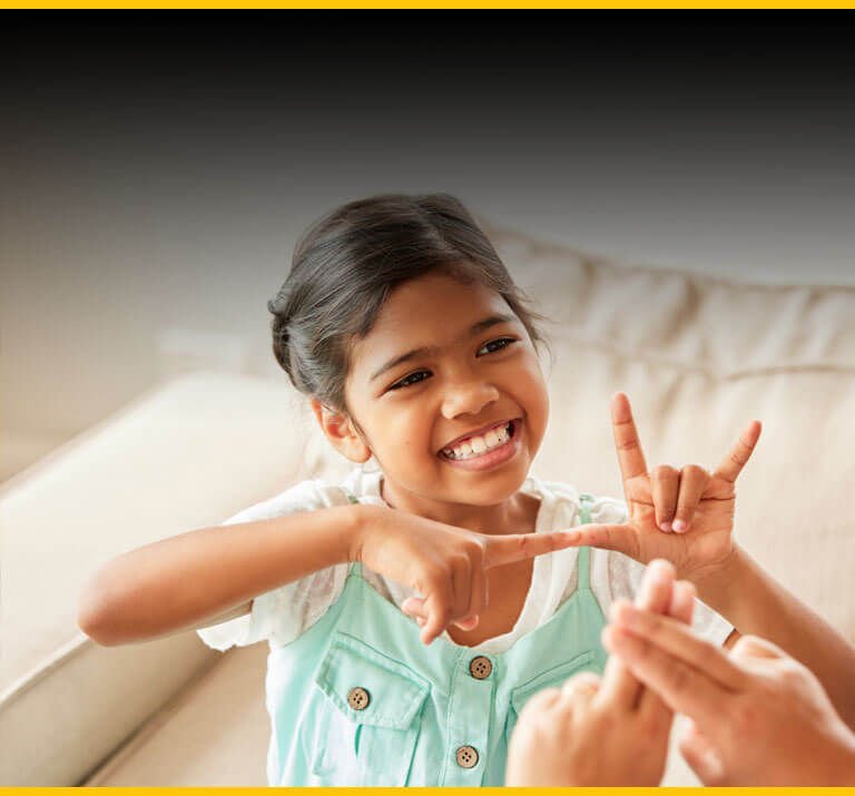 A smiling second grader carries on a conversation with her mother in sign language.