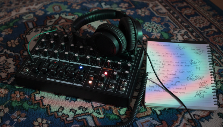Close-up of a synthesizer, lyric notebook, and headphones on a patterned rug.