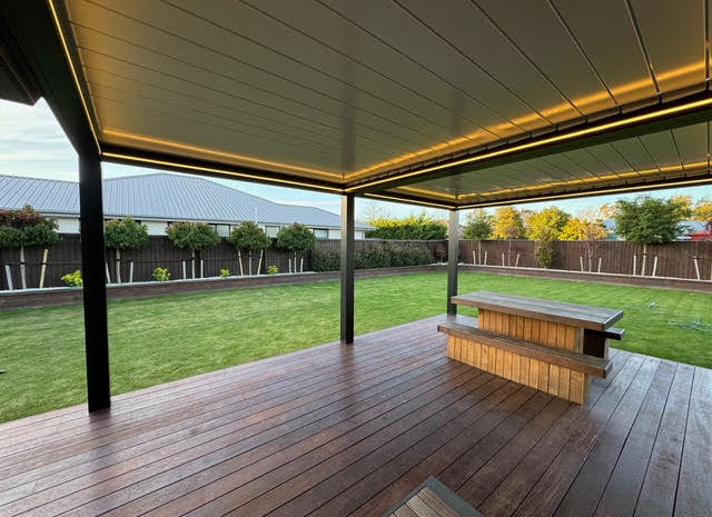 A closed Skyline Louvre with LED lights on over a wood patio, looking out over a green lawn.