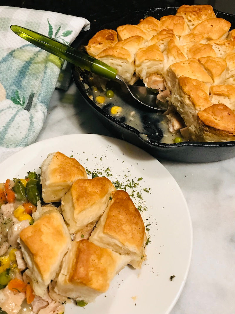 Biscuit-topped pot pie in iron skillet with a serving on white plate