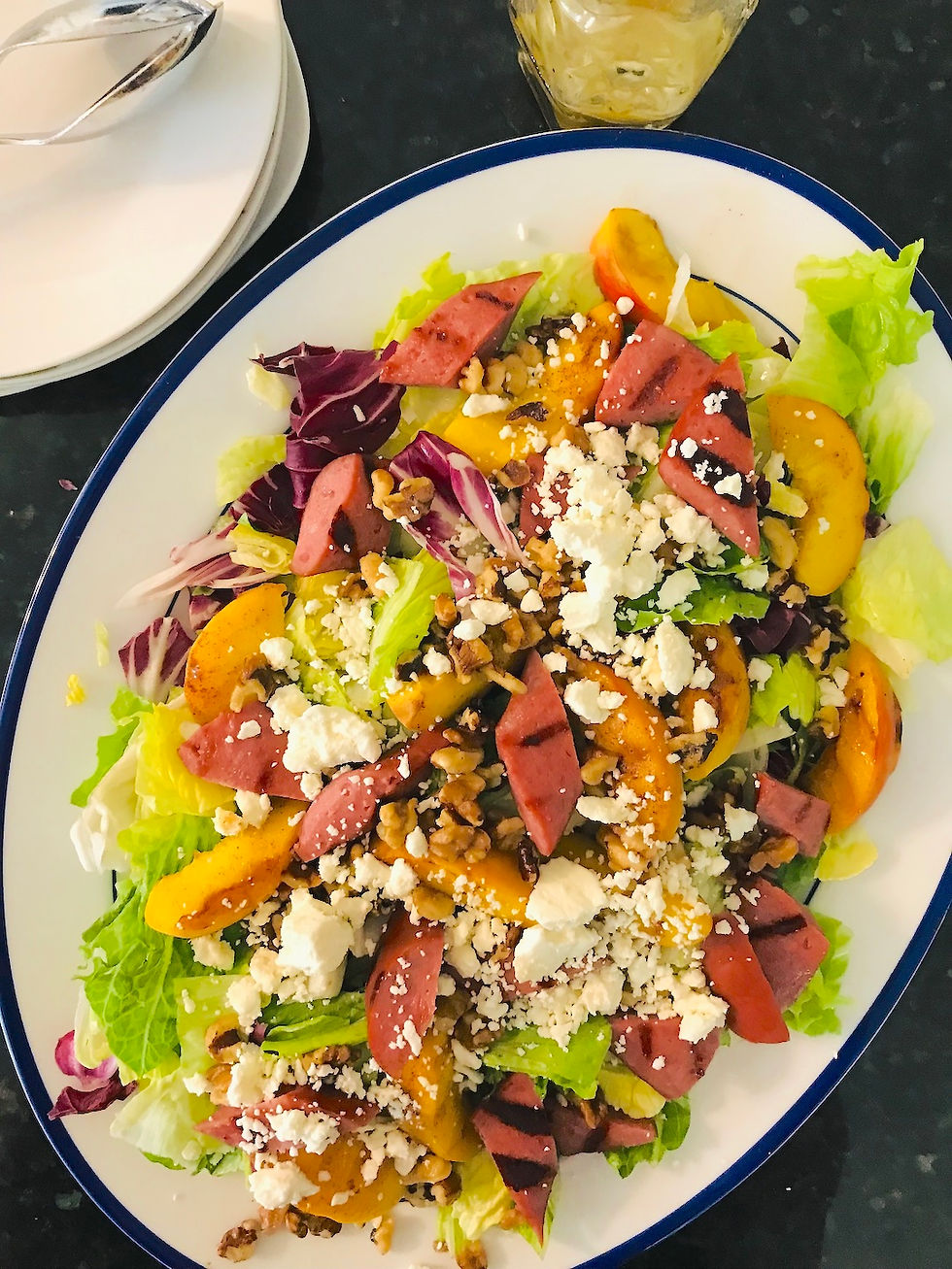 platter contains salad greens, grilled smoked sausage, peaches, feta cheese and walnuts