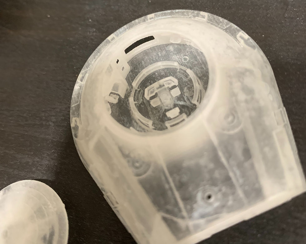 Close-up of a clear plastic cylindrical part with small tabs, resting on a dark surface.