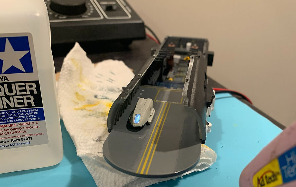 Shuttle bay on a workbench beside a Tamiya Lacquer Thinner bottle and paper towel, with a small white vehicle on deck.