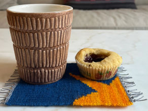 Woven mug rug on a frame loom with a coffee cup and cookie