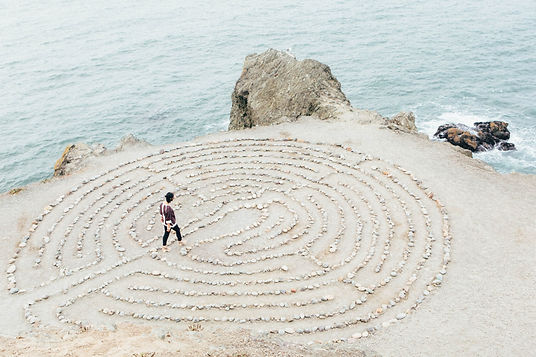 human by the coast, walking through a labyrinth drawn on the ground