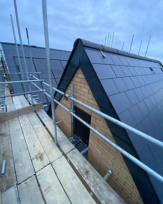 A rooftop with scaffolding, showing brickwork and black roof tiles at dusk