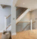 A modern staircase with wooden handrails and black vertical balusters in a bright, neutral-toned space.