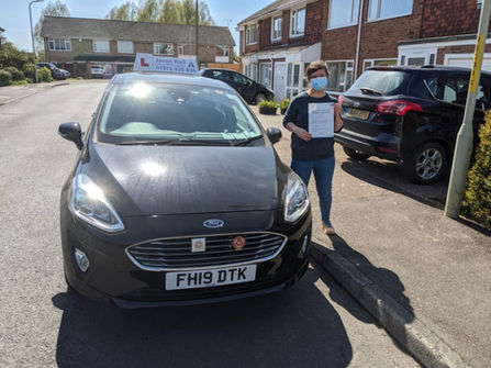Person with a certificate standing beside a car with a learner's 'L' plate.