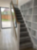 A modern staircase with shelving and a glass door.