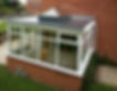 White conservatory with glass windows and a dark roof attached to a brick house