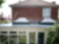 Flat roof with two skylights on a conservatory, brick house and garden in background