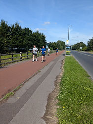 Three people running on a red paved path alongside a road