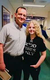 a young woman with long curly blond hair stands beside a man in a hospital hallway