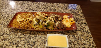 Hibachi meal featuring fried rice, shrimp, beef, vegetables, and dipping sauce.