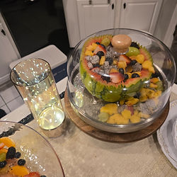 Fruit salad in watermelon half, covered, on kitchen counter, glass.