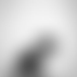 Aunty Charmaine seated in quiet stillness, head bowed in deep reflection, holding mala beads, wearing glasses and a casual outfit, captured in black and white against a soft neutral backdrop.