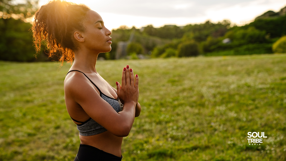 Woman standing in a sunlit field with hands in prayer position practicing going within through stillness and spiritual intention — Soul Tribe Media