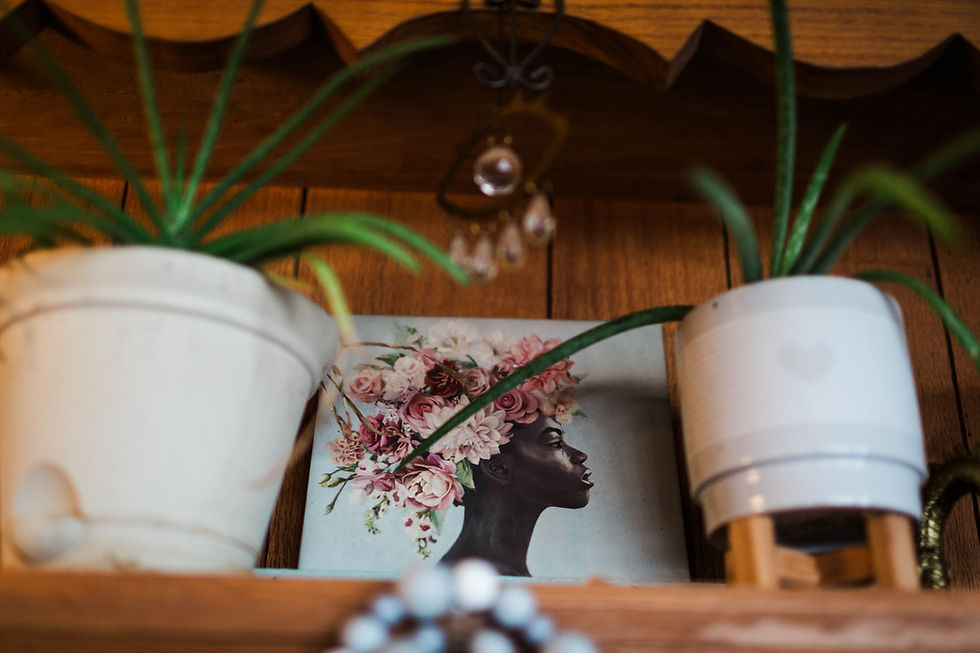 A wooden altar shelf displaying two white ceramic planters with green aloe, a crystal chandelier accent, and a framed illustration of a Black woman in profile with florals blooming from her crown.
