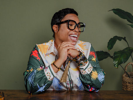 Aunty Charmaine wearing stacked crystal bracelets from Beads & Potions The Mystikal Apothecary, smiling at a wooden table with natural green plant background