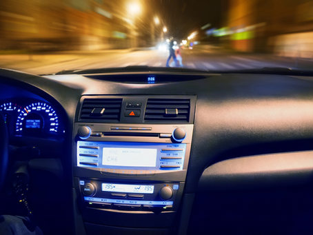 View from inside a vehicle showing the dashboard and a blurred view through the windshield of pedestrians crossing at a crosswalk at night.