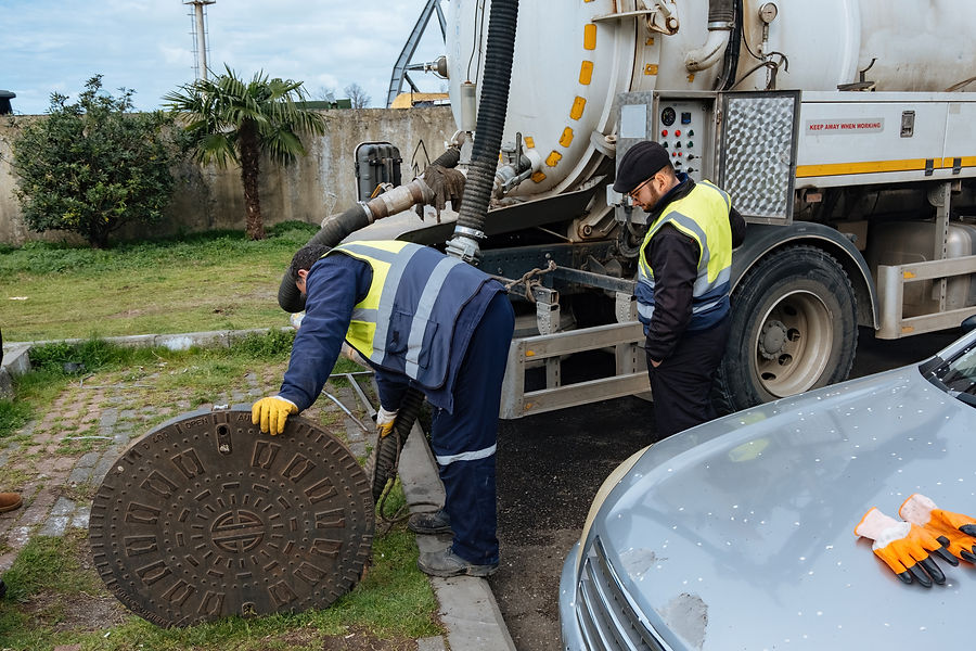 Two workers in reflective vests and gloves operate a large vacuum truck