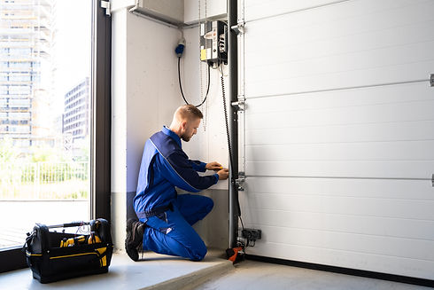 A technician in a blue uniform kneels by a garage door