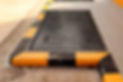 A diamond plate manhole cover bordered with worn yellow and black striped paint on concrete