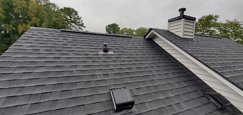 Gray shingled roof of a house with a chimney and several vents
