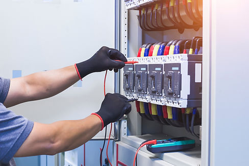 Electrician with black gloves uses a multimeter to test electrical panel connections