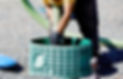 A worker in a yellow shirt and black gloves handles a green septic tank, connecting a large hose