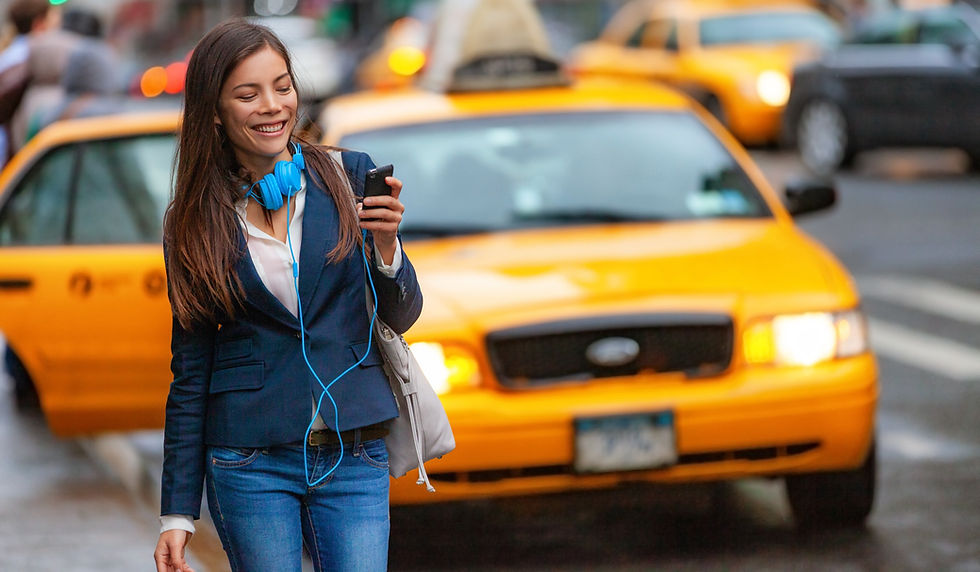 A woman wearing a smile as she glances at her phone, with yellow taxis visible in the background.