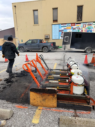 Workers repairing asphalt in a parking lot using paving equipment
