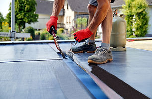 A person wearing red gloves and grey sneakers seals a roof with a blowtorch
