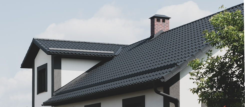 A modern house with a dark grey tiled roof and a brick chimney against a partly cloudy sky