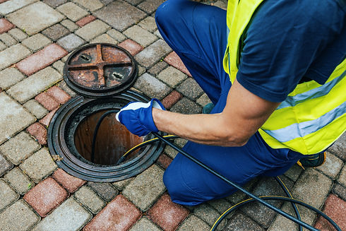 A worker in a high-visibility vest and gloves feeding a cable into an open manhole on a paved sidewalk