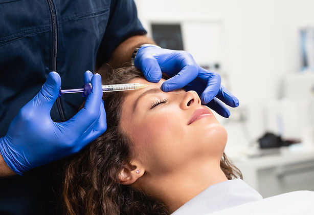 Gros plan sur les mains d'une esthéticienne injectant du botox au front d'une femme.